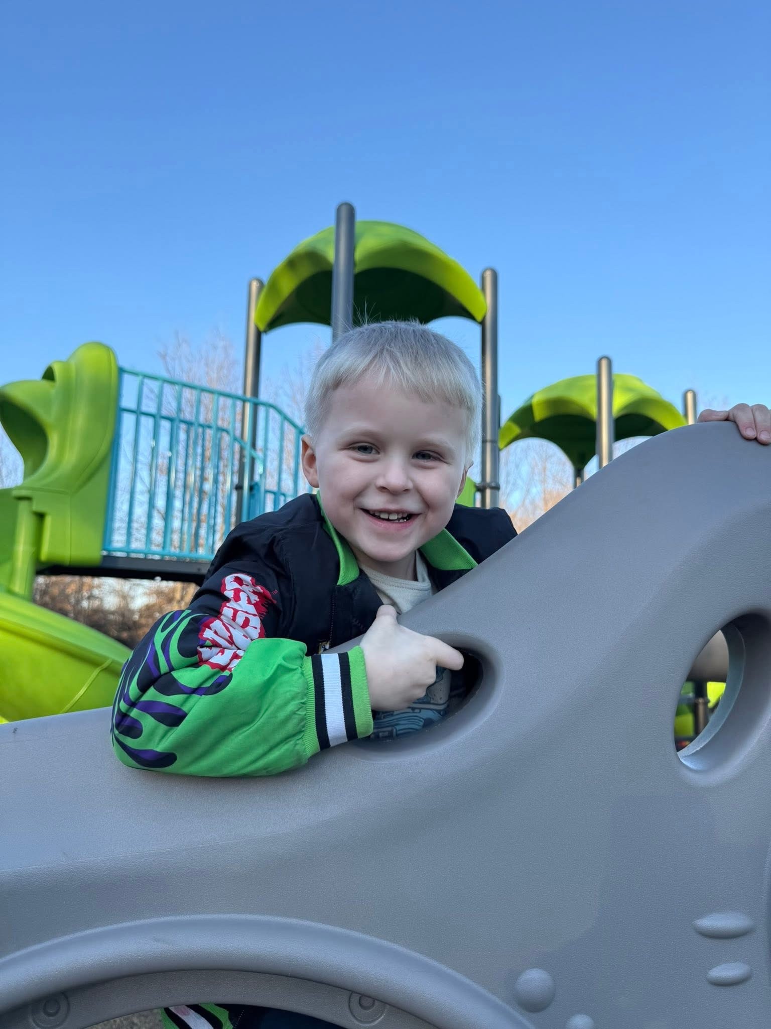 Young Discovery Program participant smiling while climbing playground equipment on a sunny day in Moberly